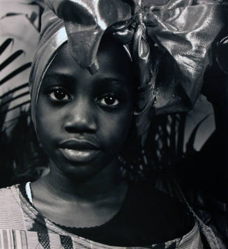 A black and white photograph of a girl with a metallic head wrap and an off-the-shoulder stripe…